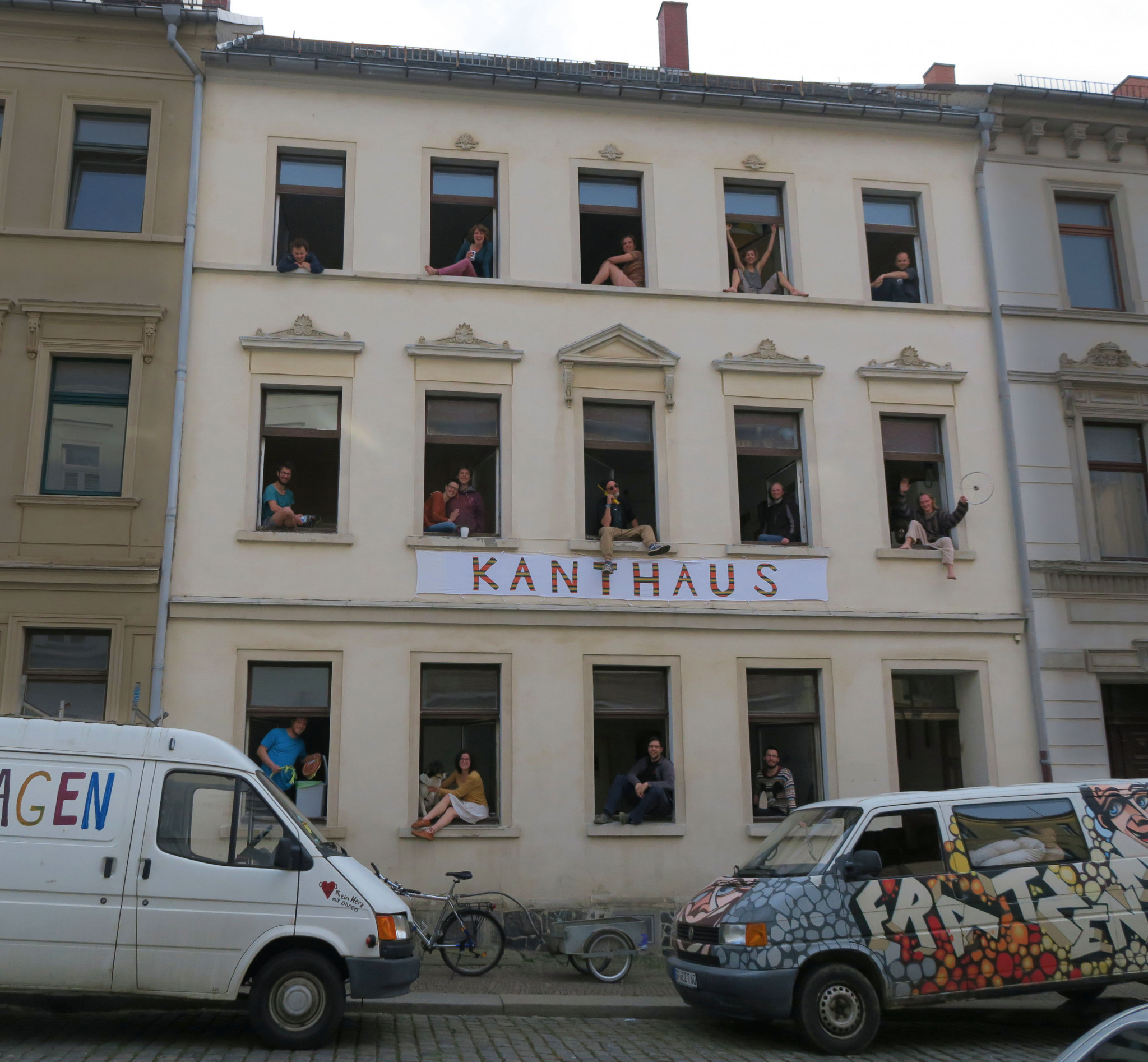 A street-view of an old building with happy people waving out of the windows.